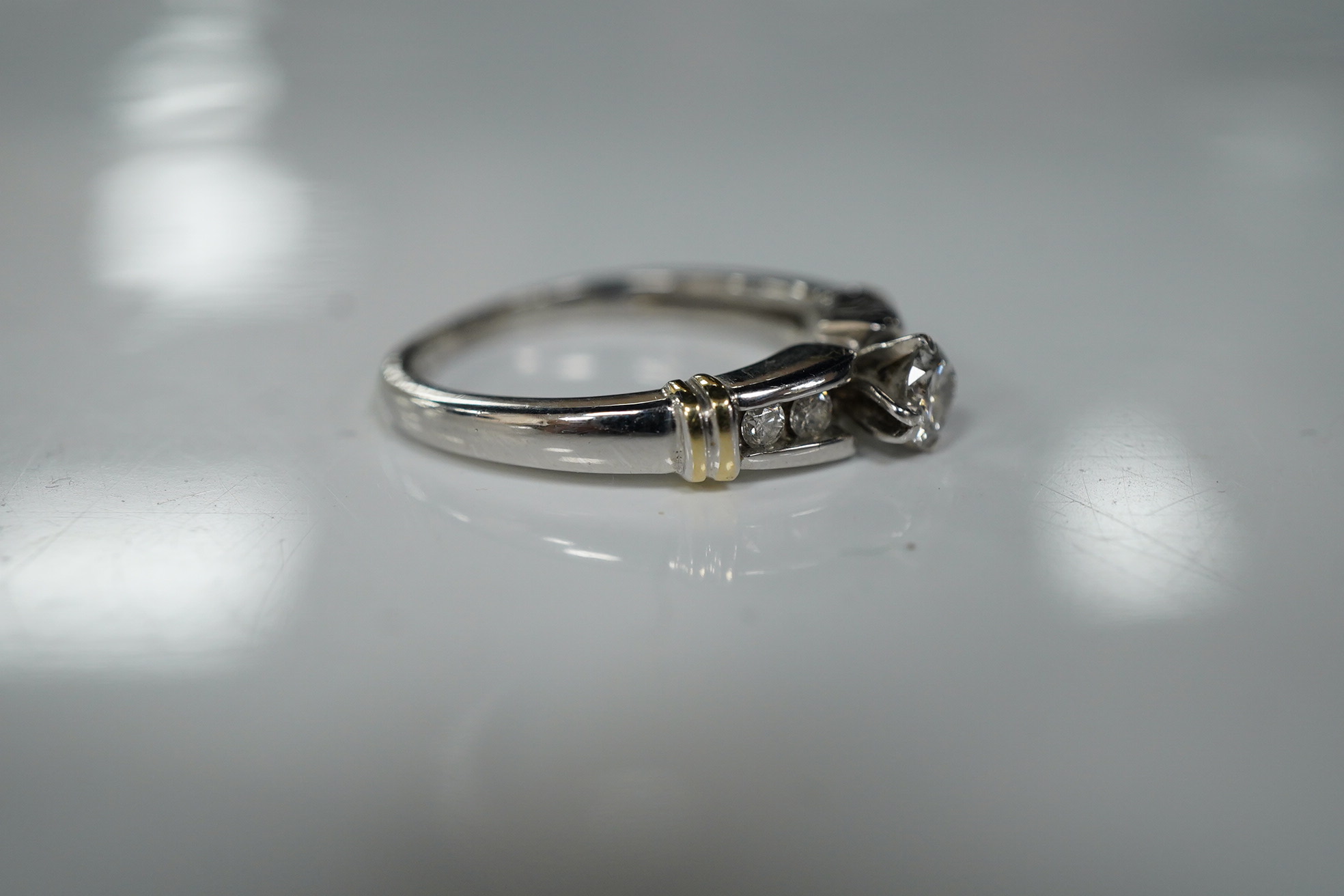 A diamond ring, claw-set with a brilliant-cut diamond weighing approximately 0.30 carats, to shoulders channel-set with smaller brilliant-cut diamonds, mounted in white gold, size R, stamped 14K, gross weight approximate